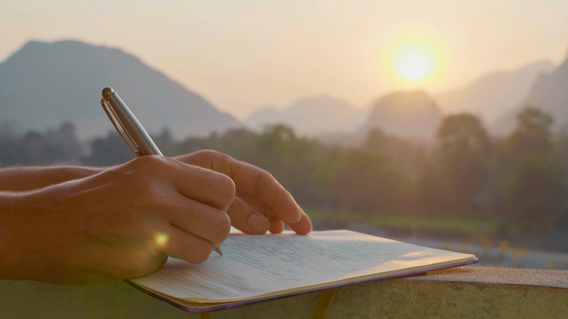 Young woman writing morning pages in diary outdoor, close-up